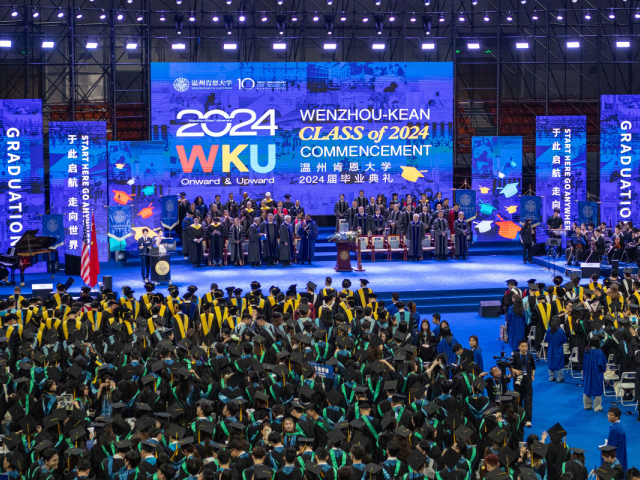 An overview photo of WKU's 2024 commencement, with students in caps and gowns, a stage of dignitaries and a sign reading WKU Class of 2024