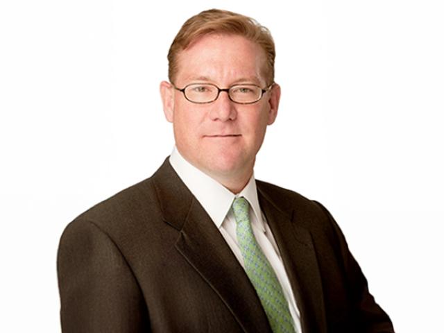 Headshot of a white male with light brown-reddish hair, glasses, wearing a dark suit, white shirt and light green tie.