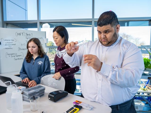 Three people; a female and a male student and a professor, conducting research in a classroom laboratory.