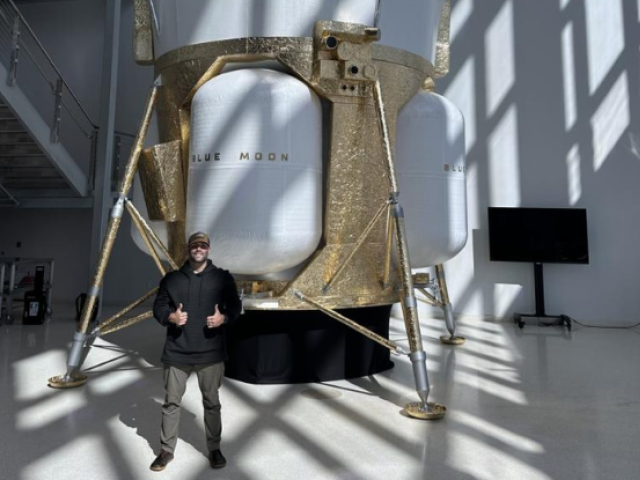 Male standing in front of a very large white and brown machine in a sunlit room.