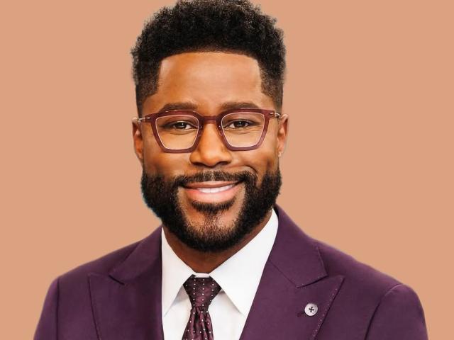 Nate Burleson smiling in a purple suit and tie with glasses, posing against a peach color background.