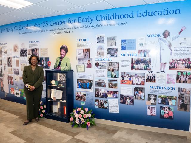 Karla Elrod standing in front of a legacy wall with images and articles about her mom, Betty C. Elrod Cobb
