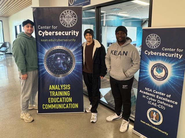 Three students in Kean's NPCIR cybersecurity program in front of banners