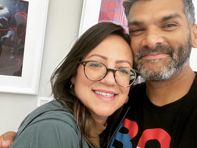 woman with dark hair and glasses posing with her husband, a male with salt and pepper hair and short beard