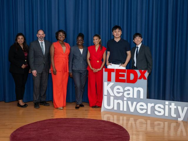 men and women lined up on a stage next to a sign reading TedxKean University