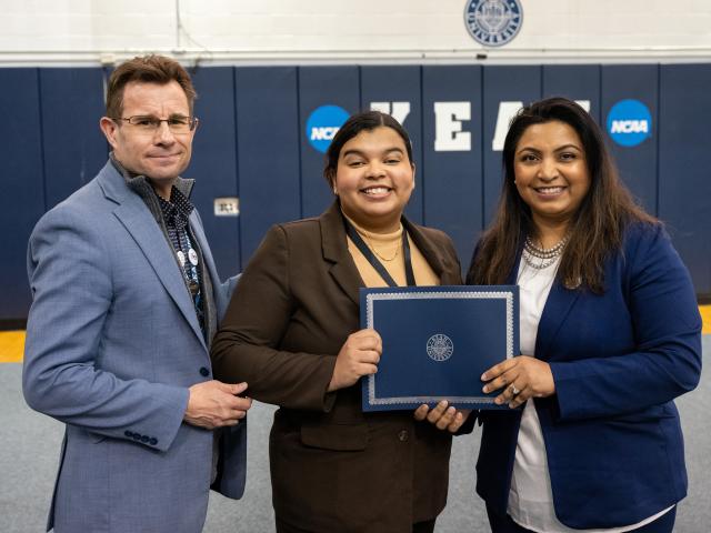 Woman holding an award standing next to another woman and a man