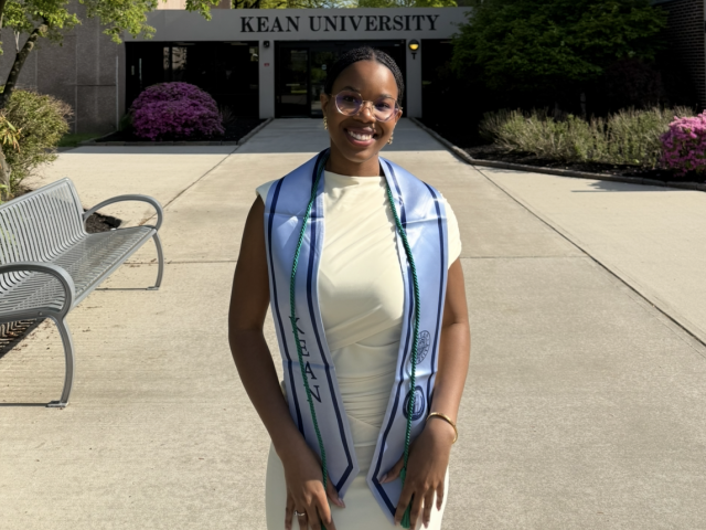 Woman in graduation attire standing in front of building at Kean