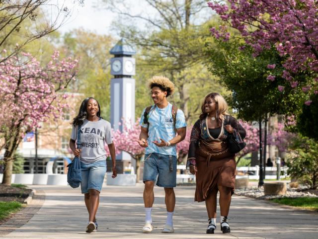 Three students walking on a sidewalk surrounded by trees