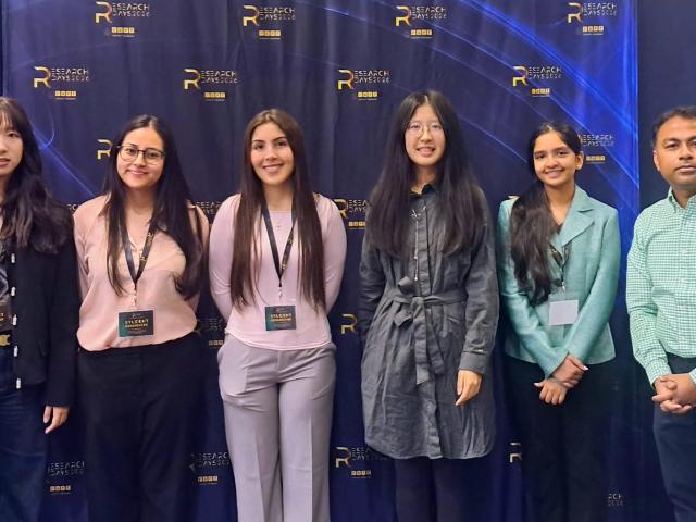 Five female students and one male professor in front of a blue backdrop