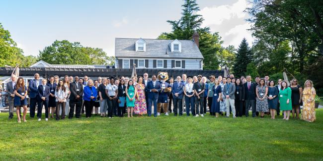 diverse gathering of new faculty with school mascot in the center on a lawn