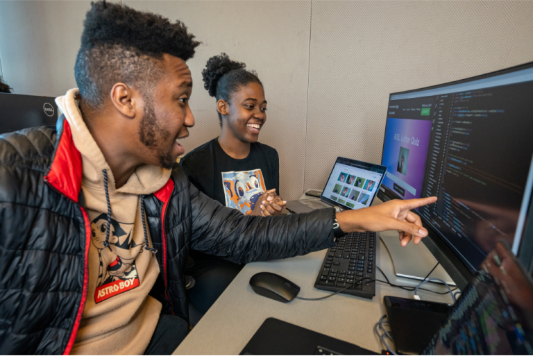 Two students working together, one pointing at a computer screen