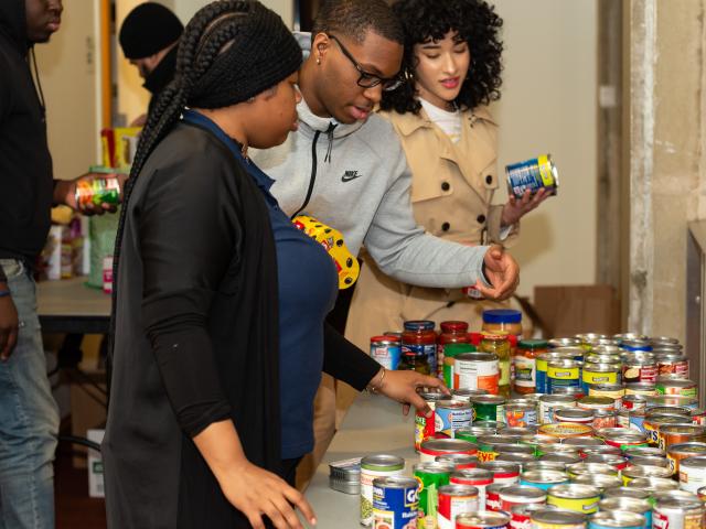 Three students organize canned goods on a table to see all of the donations for the food pantry laid out.