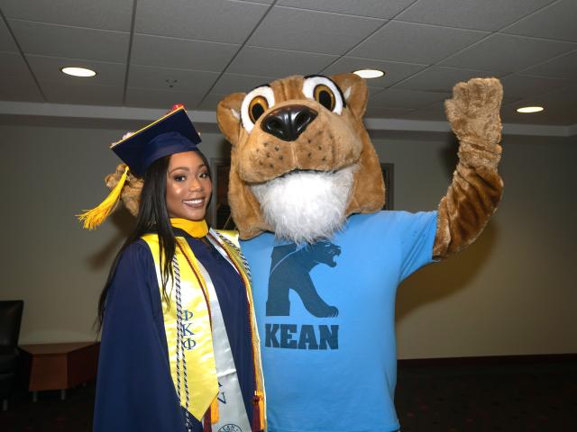 A Kean University graduate poses with the Kean cougar mascot.