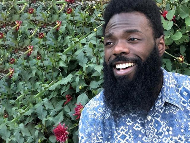 Tylie, an African American smiling to the side with flowers in the back and a blue patterned shirt