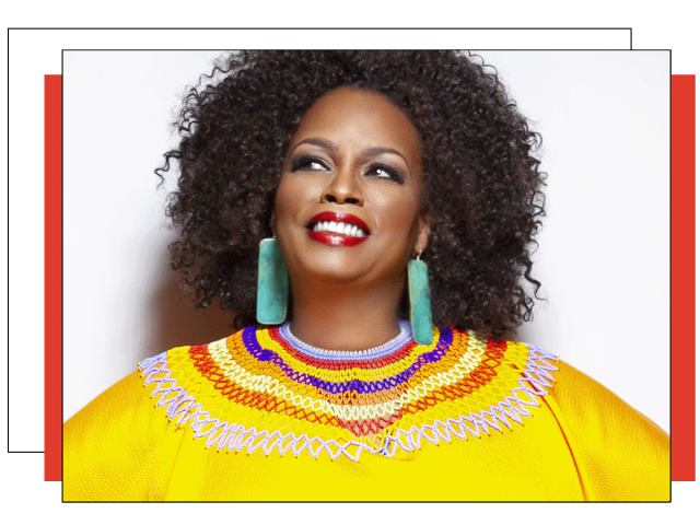 Dianne looking up while smiling. She has long green earrings, loose curly hair, big smile and yellow shirt with colored collars