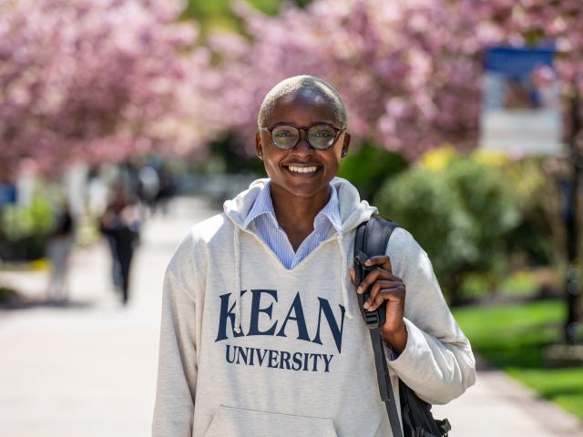 A Kean student with close cropped platinum blonde hair stands near a grove of cherry blossom trees