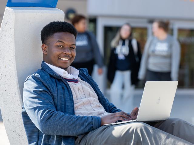 Kean student lounges in circle chair outside the Miron Student Center.