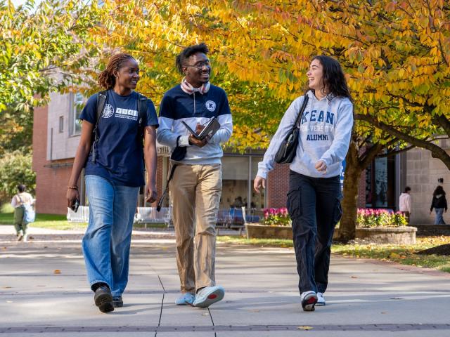 Three Kean students walk down Cougar Walk against a backdrop of fall foliage. 