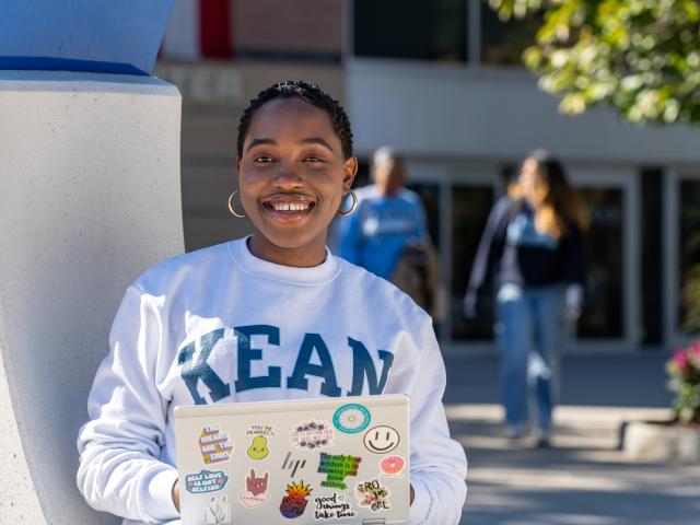 A Black student with a laptop poses on the Miron Student Center patio