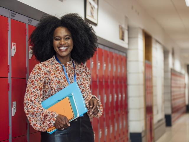 A teacher leans on a locker in an empty corridor. 