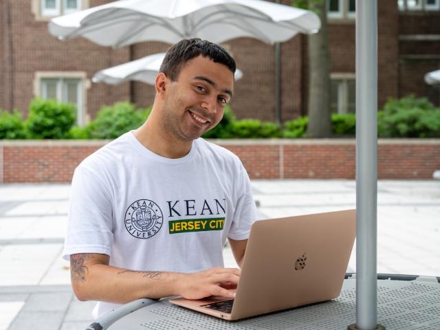 A Kean Jersey City student studies on the patio on his laptop