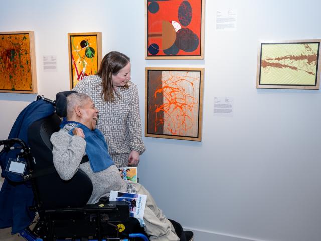 A wheelchair bound art lover view an art exhibition accompanied by a guide