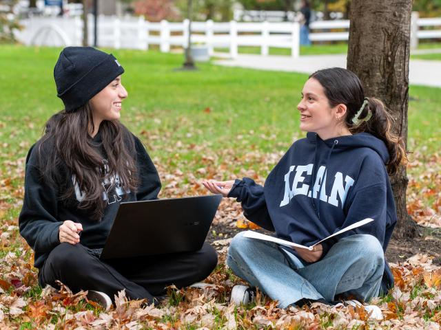 Kean students sit in a leaf mound studying