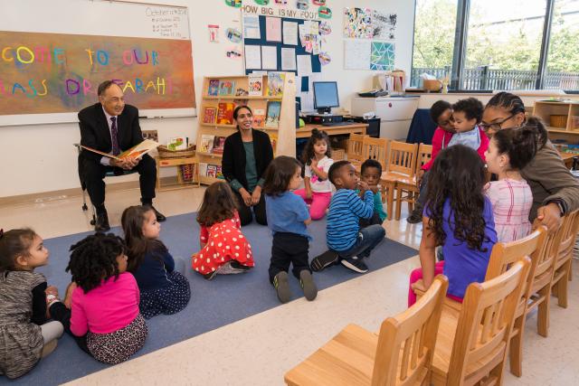 Dr. Farahi has a book open and stops his reading to talk to a child. 