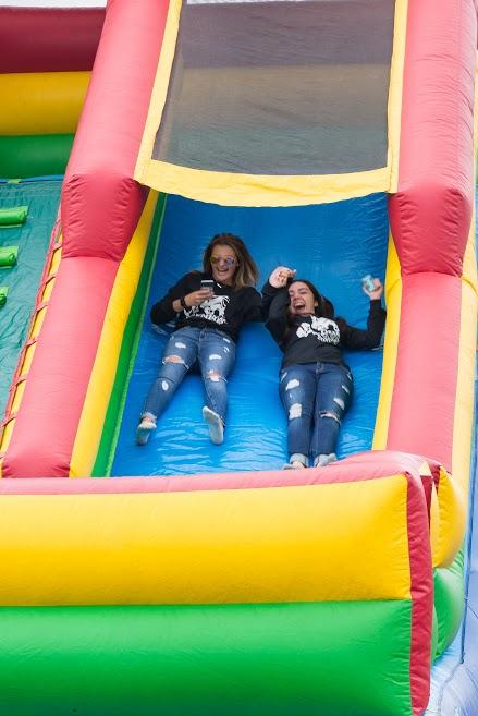 Two girls slide down a bouncy house slide. 