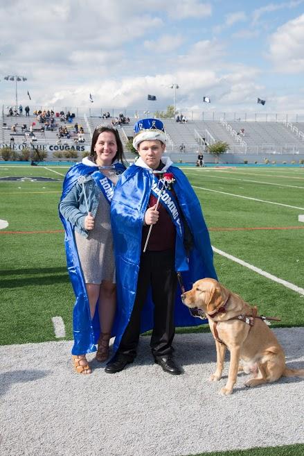 The homecoming king and queen pose for a picture with a service dog by the Homecoming King's side. 