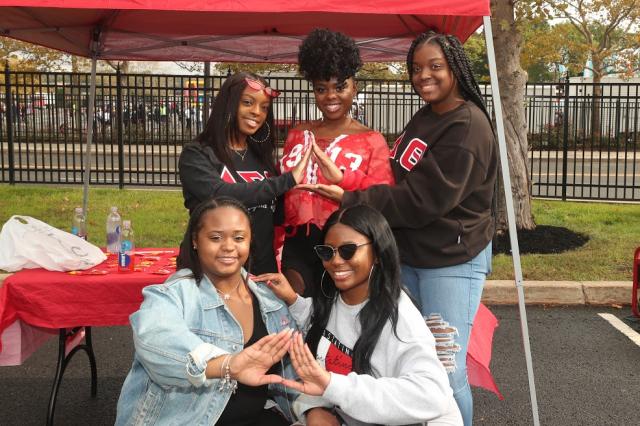 Five sorority sisters pose for a picture holding up their sorority hand signs. 