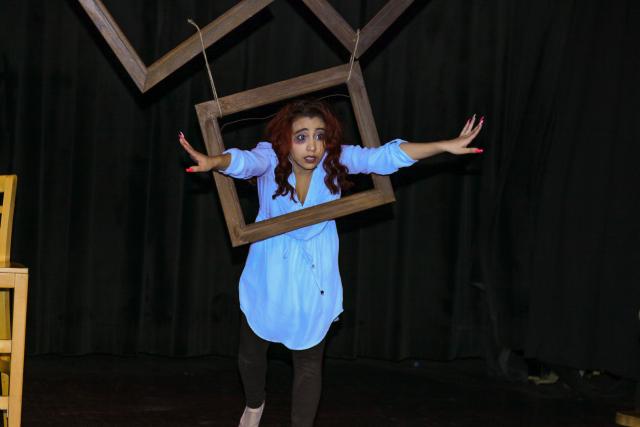 An actress on stage poses through a hanging, open window.