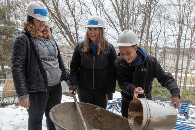 Three students mix the stucco in a wheelbarrow 