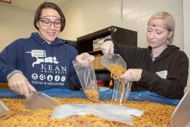 Two students chat while bagging pasta.