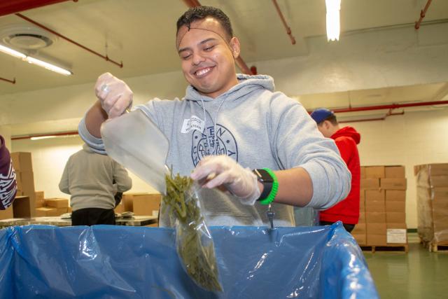 Student volunteer uses a scoop to put pasta in plastic bags