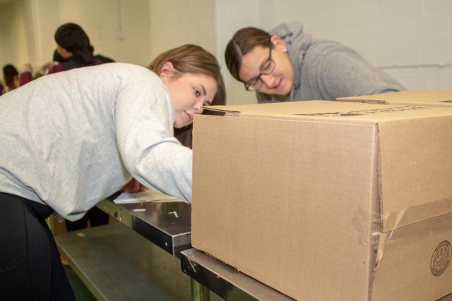 Two students stuff boxes filled with pasta to send