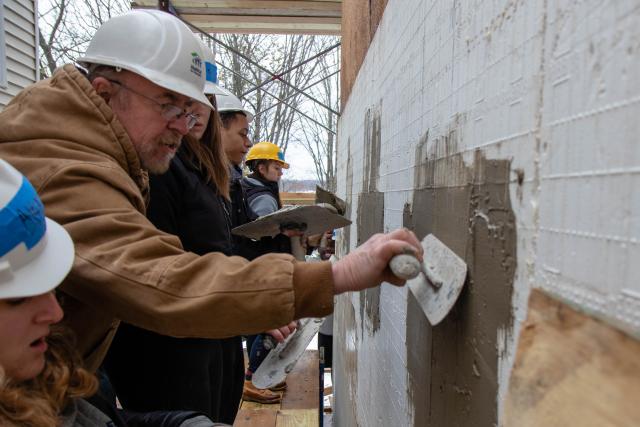 The site manager, Bob at Habitat for Humanity uses tools to show students how to stucco the side of the house.