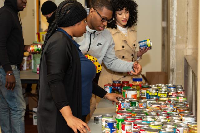 Three students organize canned goods on a table to see all of the donations for the food pantry laid out.