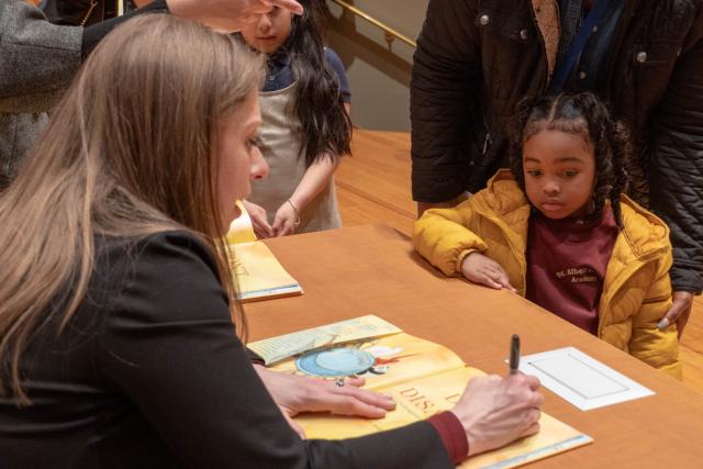 Clinton signs a book for a young girl who looks on. 