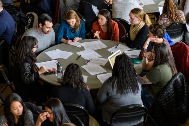 Students gather around at a table looking at paperwork. 