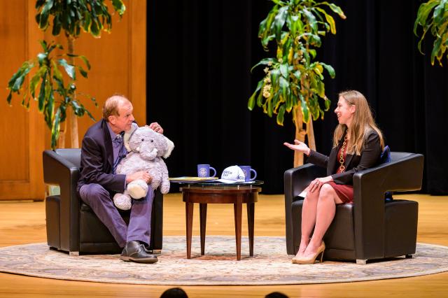 Senator Lesniak and Chelsea Clinton discuss endangered animals on while seated on stage as Lesniak holds a stuffed elephant. 