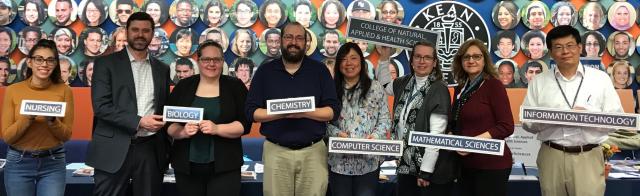 Photo of College of Natural, Applied and Health Sciences faculty and staff holding signs representing their disciplines at the Open House Expo