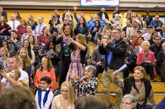 A large crowd of parents stand to cheer and take photos of their children who are a part of the honors convocation