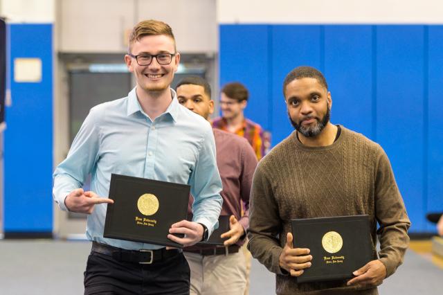 Two students stand side by side, displaying their diploma covers at the honors convocation 