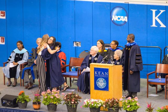 Student board of trustee hugs her fellow coworker from the center for leadership and service on stage at the honors convocation