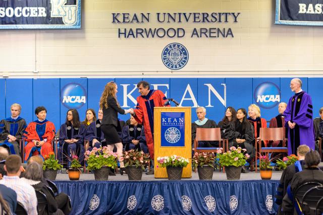 Student walks across stage and shakes hand with the Dean of her college prior to accepting her honors degree