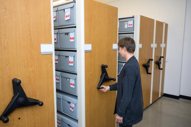 This is an image of Kean Archivist Erin C. Alghandoor using the compact shelving in Research Library 