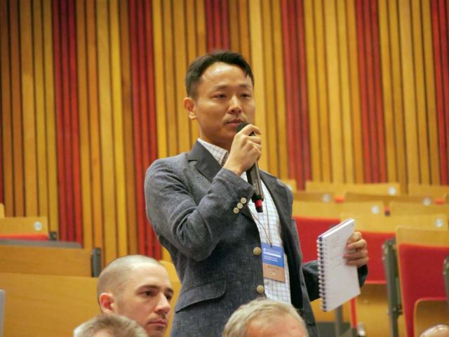 Kean University assistant professor Bok Jeong holding a microphone and speaking at an event.