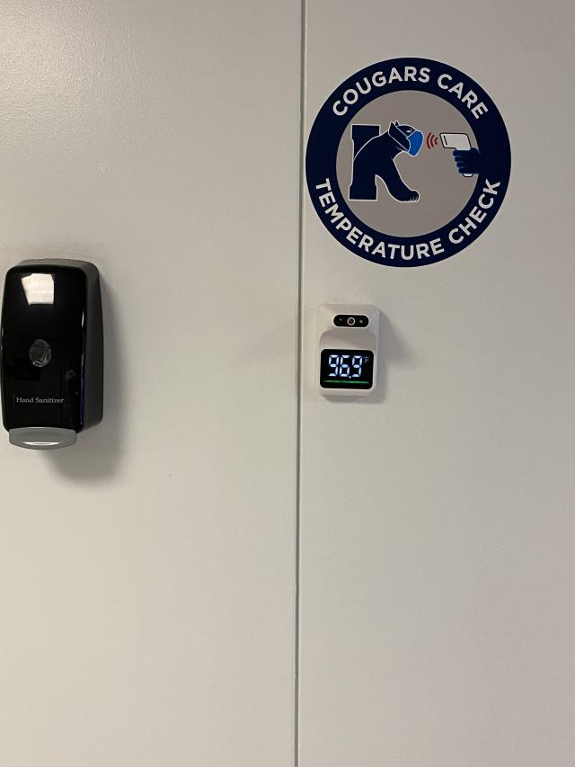 Photo of self check thermometers and hand sanitizer Cougar Care sign