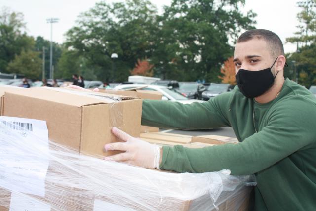 Student assisting by carrying boxes at food distribution on campus.